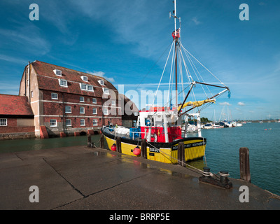 Gelbe kommerziellen Shell Fischkutter vertäut Kai am Ashlett am Southampton Water mit alten Mühle rote Backsteingebäude Stockfoto