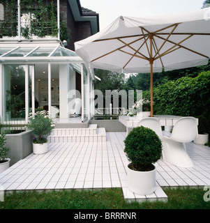 Großen weißen Schirm oben weiße Stühle und Tisch auf weiß gefliesten Terrasse mit beschnittenen Box in weißen Töpfen Stockfoto