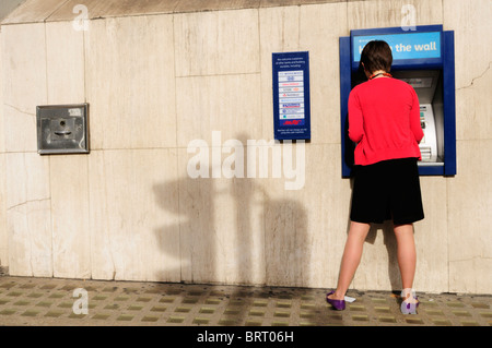 Eine junge Frau Geldabheben von einem Barclays Bank Loch in der Wand Geldautomaten, London, England, UK Stockfoto