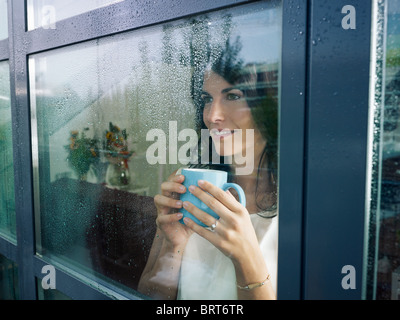 Mitte Erwachsene Frau Kaffee trinken und Blick aus dem Fenster an regnerischen Tag. Horizontale Form Stockfoto