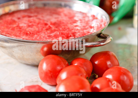 Tomaten auf einem Sonnenlicht Küche Marmor Arbeitsfläche vor einem Stahl Topf voller Tomatensaft. Stockfoto