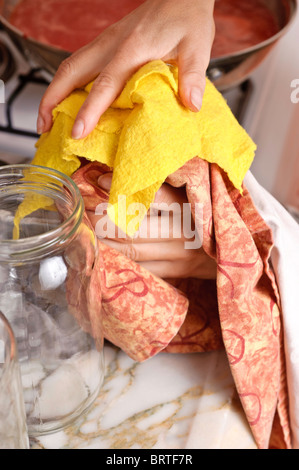 Eine Frauenhand ziehen Sie den Deckel auf einem heißen Glas mit einem Tuch und Geschirrtuch um vor der Hitze schützen Stockfoto