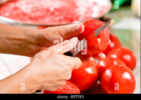 Eine Frauenhand verwenden Sie ein Messer zum Schälen der Haut aus einer Tomate. Anderen Tomaten sind auf einem Sonnenlicht Marmor Küchenarbeitsplatte Stockfoto