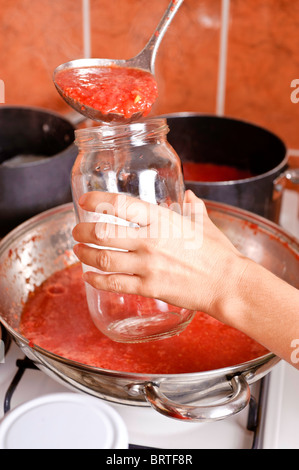 Die Hand einer Frau hält eine leere Glas während beheizten Tomatensaft aus einer Pfanne, über einem Topf gießen. Stockfoto