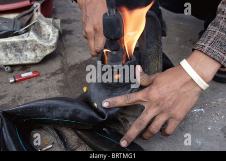 Ein Bürgersteig Reifen Mechaniker nutzt Feuer Kautschuk zu schmelzen, während Befestigung ein Innenrohr an einer Straßenecke in Phnom Penh, Kambodscha. Stockfoto