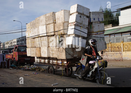 Eine Lieferung Mann auf einem Motorrad wird auf seinem Weg mit einer großen Belastung von Boxen auf einer Straße in Phnom Penh, Kambodscha gestoppt. Stockfoto