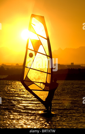 Silhouette der Mann über das Segeln Windsurfen in strahlendes Licht des Sonnenuntergangs Stockfoto