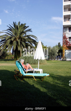 ÄLTERE URLAUBERIN, DIE SICH IN EINEM HOTELGARTEN ENTSPANNEN. Stockfoto