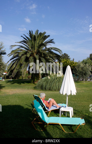 ÄLTERE URLAUBERIN, DIE SICH IN EINEM HOTELGARTEN ENTSPANNEN. Stockfoto