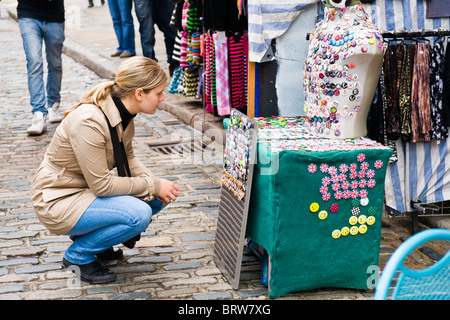 Camden Town Markt Lock, duckt sich hübsche junge Blondine in Lederjacke & Jeans durch Anzeige der Auswahl von Neuheit Abzeichen Stockfoto