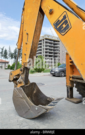 Die Klaue von einem gelben JCB Bagger ruht auf der Straße vor einer Wohnung Entwicklung vor Ort. Stockfoto