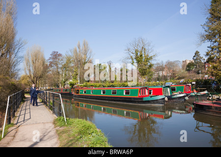 Menschen zu Fuß auf Uferweg neben Fluss Wey mit Kanalboote vertäut am Godalming Navigation in Guildford Surrey England UK Stockfoto