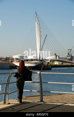 Junge Frau, die an die neue Schaukel Fußgängerbrücke im Bau an der MediaCityUK Komplex, Salford Quays, Manchester, UK Stockfoto