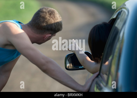 Junge Frau zeigte vom Auto mit jungen Mann gelehnt, Auto Stockfoto