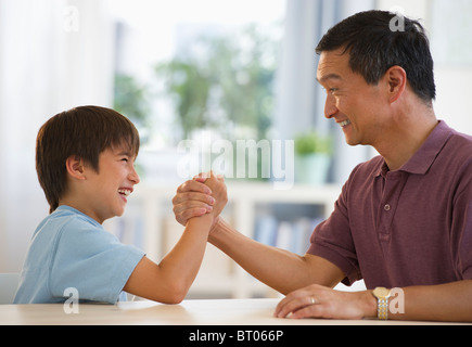 Vater und Sohn Armdrücken am Tisch lächelnd Stockfoto