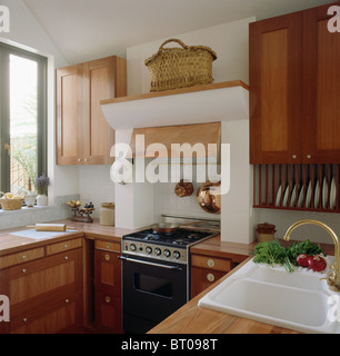 Korb auf Regal über schwarze Ofen in kleine Küche mit hellem Holz ausgestattet und Schränke und weißen Doppel-Waschbecken Stockfoto