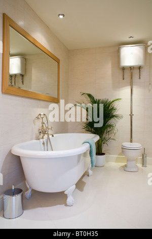 Große Holz eingefassten rechteckigen Spiegel über Roll-Top Bad in Creme geflieste Badezimmer mit hohen Zimmerpflanze neben WC Stockfoto