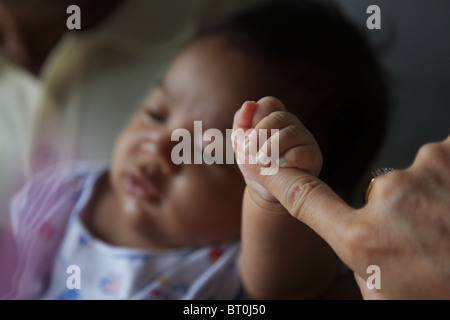Eine Nahaufnahme von einen 2 Monate alten thailändischen muslimischen jungen halten, um einen Erwachsenen Finger
