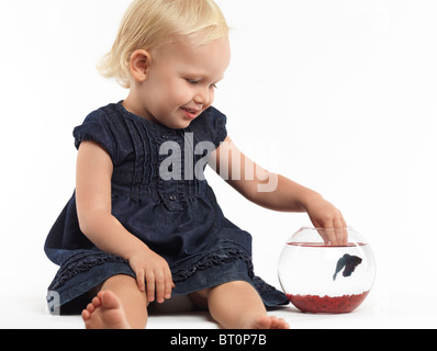 Porträt von einem lächelnden zwei Jahre alten Mädchen spielen mit einem Fisch in eine Schüssel geben, die isoliert auf weißem Hintergrund Stockfoto