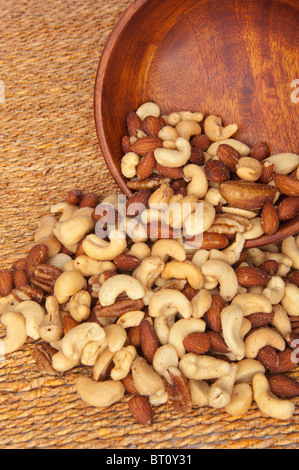 Eine verschüttete Holzschale gemischte Nüsse, wie Walnüsse, Haselnüsse, Mandeln und Cashew-Kerne. Stockfoto