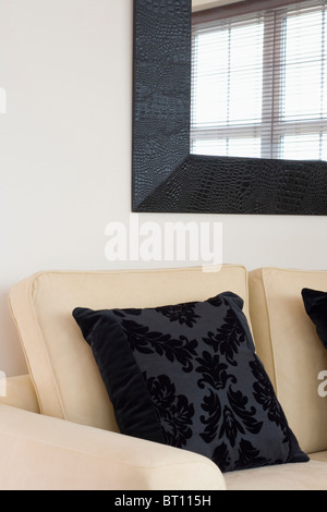 Nahaufnahme der Creme Sofa mit gemusterten schwarzen Kissen unter Spiegel Stockfoto