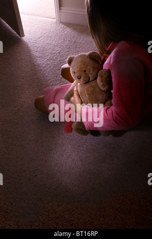 Kleines Mädchen allein in einem dunklen Raum mit einem Teddybär, Rückansicht. 3 Stockfoto