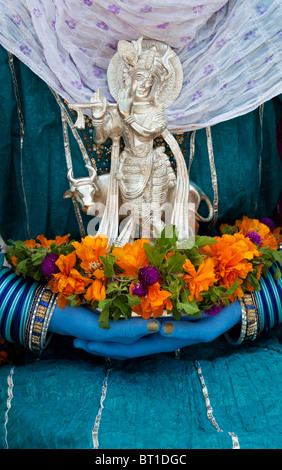 Indische Mädchen, dass eine Silber Krishna Statue und Blumen mit blauen Händen. Indien Stockfoto