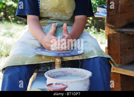 Lehrling macht Keramik durch das werfen Rad. Er trägt Jeans, T-shirt und Schürze mit Ton gefärbt. Stockfoto