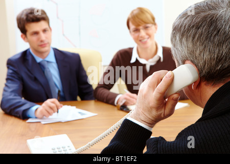 Rückansicht des Bankangestellten ruft auf dem Handy gegenüber zwei Besucher Stockfoto