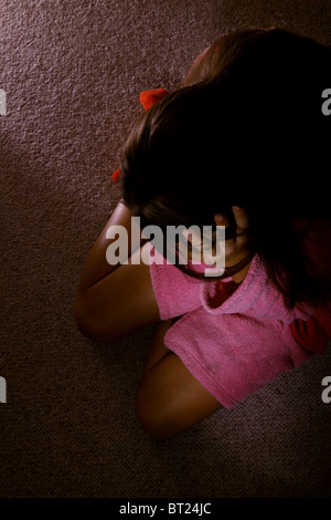 Mädchen tragen einen Morgenmantel, sitzt auf einem Teppichboden mit dem Kopf in die Hände. Stockfoto