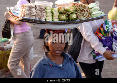 Eine Frau, die als Lebensmittel Anbieter arbeitet gleicht einem Tablett auf dem Kopf am Ufer des Mekong-Flusses in Phnom Penh, Kambodscha. Stockfoto