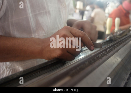 Ein junger Mann der Khmer nutzt seine Hände mit Präzision, während der Arbeit an seiner Maschine in einer Textilfabrik in Kambodscha. Stockfoto