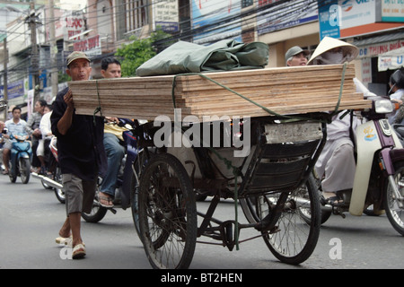 Ein asiatischer Mann spaziert im dichten Verkehr mit einer Last von Holz auf einer belebten Straße in Vietnam Saigon (Ho-Chi-Minh-Stadt). Stockfoto