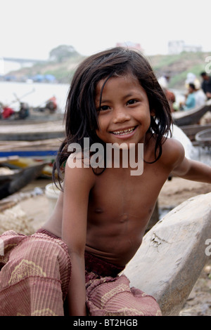 Eine junge Asiatin, die in Armut lebenden sitzt auf einem Holzboot lächelnd am Ufer des Mekong-Flusses im ländlichen Kambodscha. Stockfoto