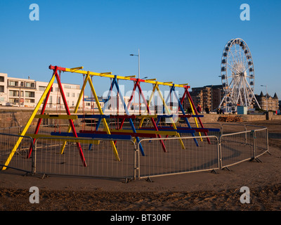 Kinder Schaukeln und das Rad von Weston an der Küste von Weston-super-Mare bei Sonnenuntergang, North Somerset, England. Stockfoto