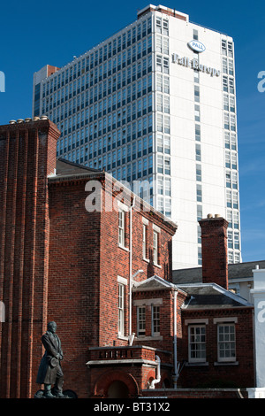 Hohes Bürogebäude mit Gebäuden der Portsmouth Historic Dockyard mit Statue von Captain Scott im Vordergrund standen. Stockfoto