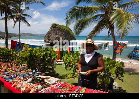 Einheimische Frau mit Souvenirs in Bathsheba Beach mit dem Pilz-Felsen im Hintergrund Stockfoto