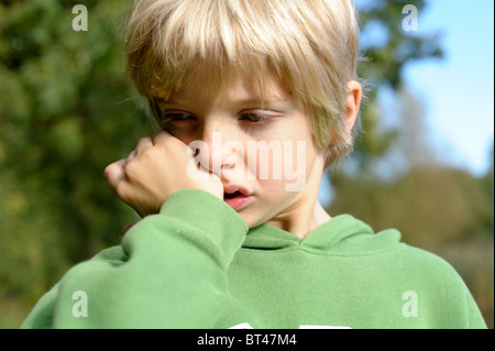 Traurig, müde und weinerlich blonden kleinen Jungen in eine grüne Spitze draußen allein nach gemobbt von Freunden zu spielen Stockfoto