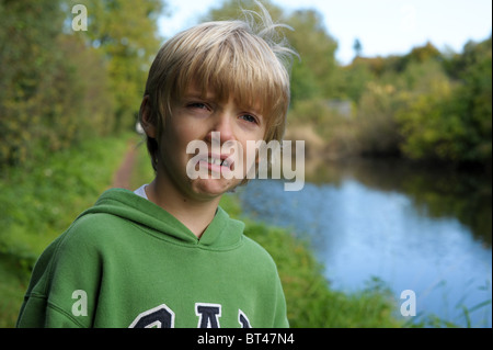 Traurig, müde und weinerlich blonden kleinen Jungen in eine grüne Spitze alleine draußen, nachdem er gemobbt und nahm am Stockfoto