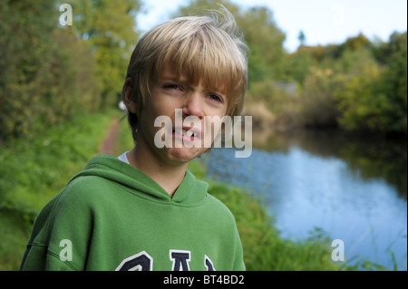 Traurig, müde und weinerlich blonden kleinen Jungen in eine grüne Spitze alleine draußen, nachdem er gemobbt und nahm am Stockfoto