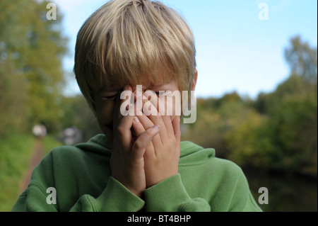 Traurig, müde und weinerlich blonden kleinen Jungen in eine grüne Spitze alleine draußen, nachdem er schikaniert und von einer Bande auf abgeholt Stockfoto