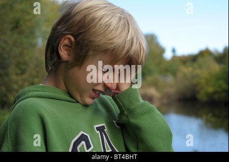 Traurig, müde und weinerlich blonden kleinen Jungen in eine grüne Spitze alleine draußen, nachdem er gemobbt und nahm am Stockfoto