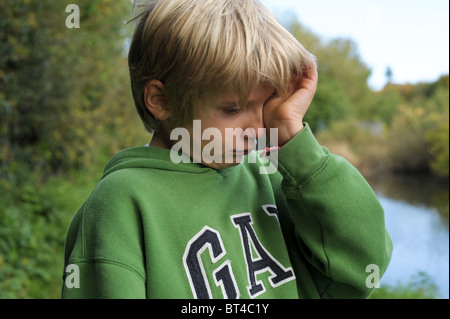 Traurig, müde und weinerlich blonden kleinen Jungen in eine grüne Spitze alleine draußen, nachdem er gemobbt und nahm am Stockfoto