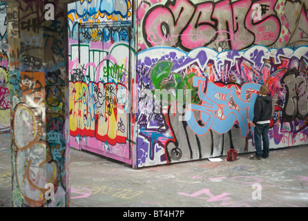 Ein Teenager malt Graffiti in der Skateboard Haven unter Queen Elizabeth Hall auf der South Bank in London, Vereinigtes Königreich. Stockfoto