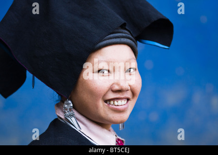 Einer schwarzen Dzao Frau tragen traditionelle Kleidung Lächeln für die Kamera, während sie vor einer blauen Wand steht Stockfoto