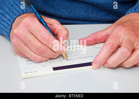 Nahaufnahme einer reifen Frau einen Scheck (Scheck) in einem Scheckbuch schreibt, eine Rechnung zu bezahlen. England, UK, Großbritannien. Stockfoto