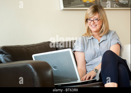 Hübsche junge Frau mit Brille, die mit einem Laptop-Computer zu Hause. Stockfoto