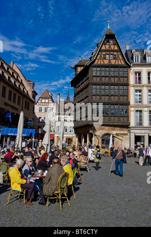 Menschen sitzen auf Café-Terrassen am Domplatz von Straßburg, Elsass, Frankreich. Im Hintergrund Wahrzeichen Kammerzell Haus Stockfoto