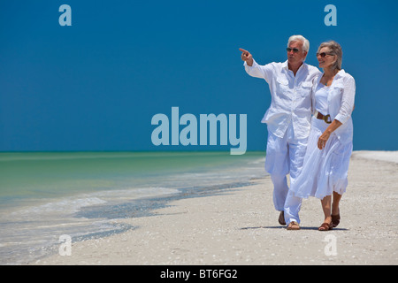 Glückliche senior Mann und Frau-Paar, gehen gemeinsam auf See auf einem einsamen tropischen Strand mit hellen klaren blauen Himmel Stockfoto