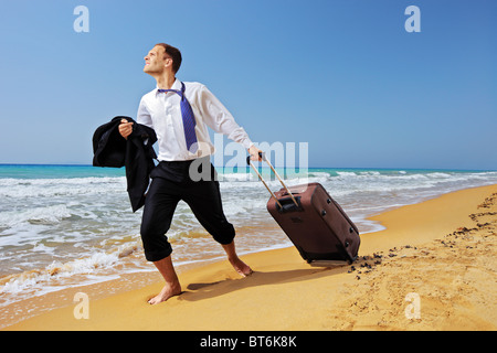 In voller Länge Portrait eines verlorenen Geschäftsmannes tragen einen Koffer am Strand Stockfoto